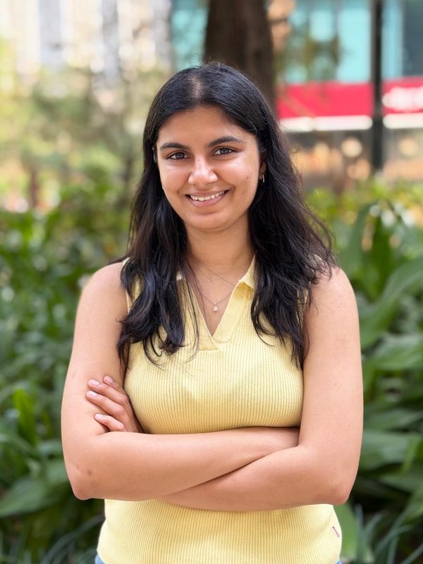 Portrait of Suhani Katariya, smiling, standing outdoors with arms folded